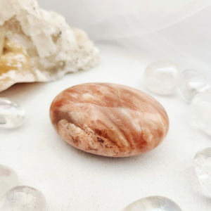 Smooth oval pink calcite palm stone with soft peach striped banding.