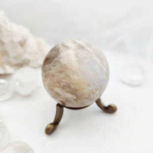 Cream-toned caramel moonstone sphere resting on a slender bronze stand.