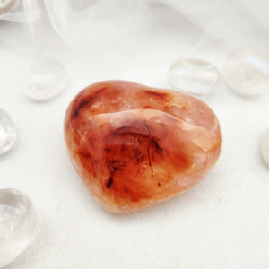 Polished carnelian heart with warm orange tone and dark inclusions