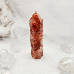 Polished fire quartz point with a tall faceted form and warm red tone