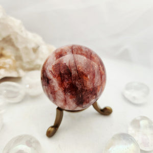 Reddish-brown fire quartz sphere resting on a slender bronze stand.