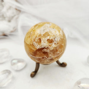 Golden crystal sphere with rugged druzy patch resting on bronze stand.