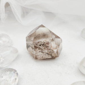 Polished lodolite quartz point with faceted form and internal mineral inclusions