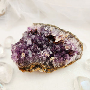 A natural amethyst crystal cluster with prominent purple crystals and a brown textured outer base