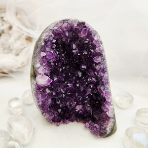 A polished amethyst geode specimen with a deep purple crystal interior and a smooth gray-brown outer base