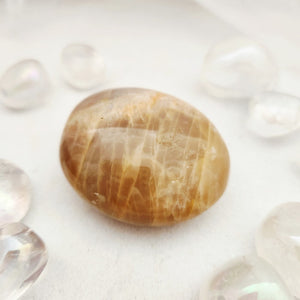 Smooth peach moonstone palm stone with warm golden-brown banding