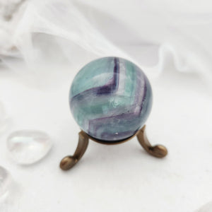 Green and purple fluorite sphere with bold banding on bronze stand.