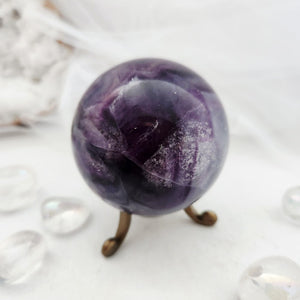 Deep purple fluorite sphere with pale banded layers on bronze stand.