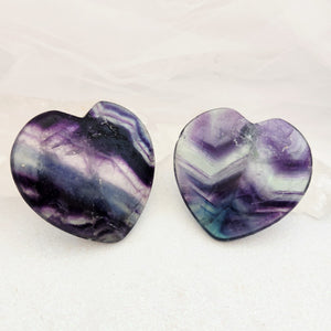 Polished rainbow fluorite hearts showing bands of purple, green, and clear crystal on a surface.