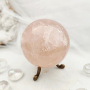 Pale pink rose quartz sphere resting on a slender bronze stand.